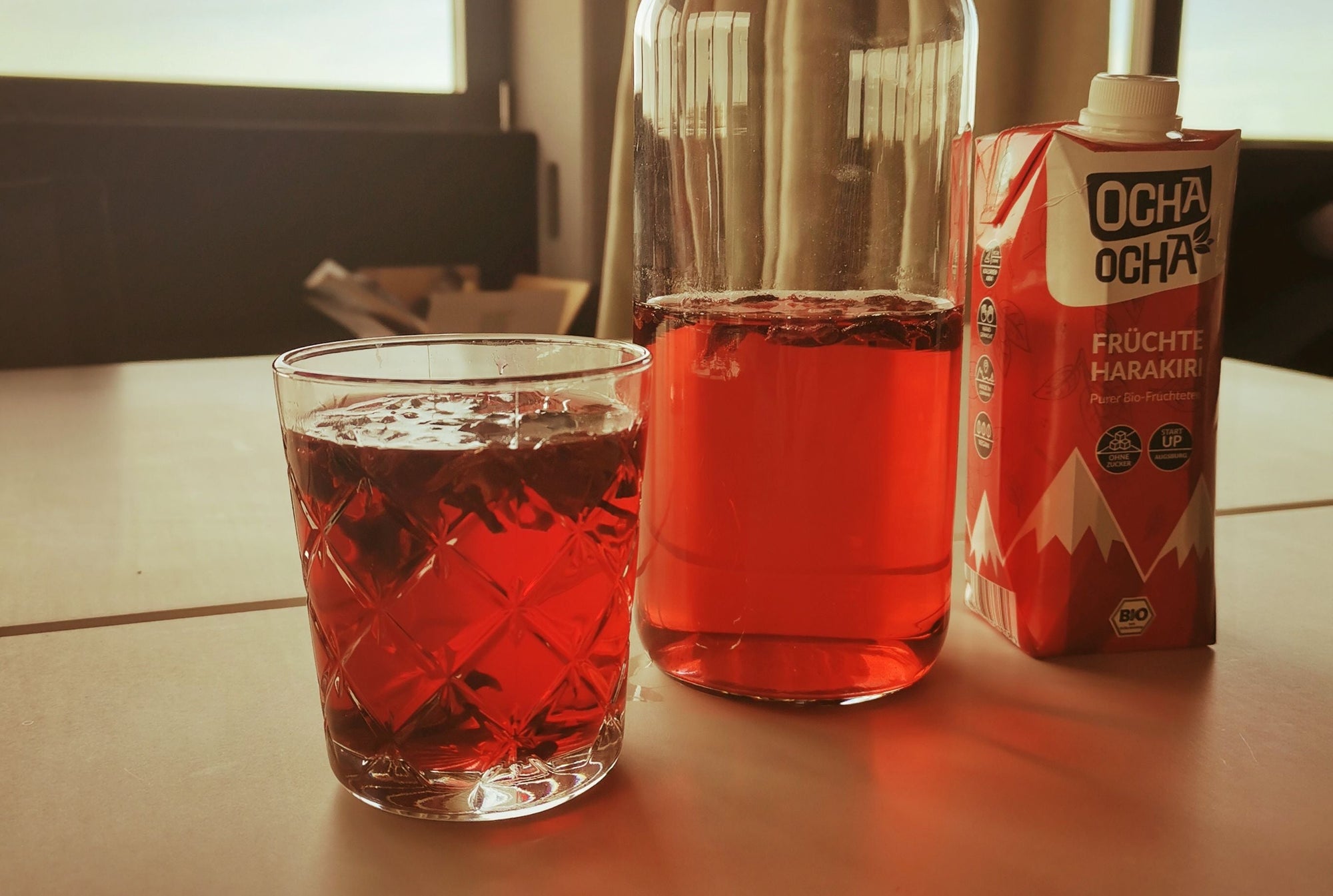 Ocha-Ocha Früchtetee im Glas und in er Wasserkaraffee, daneben im TetraPak.