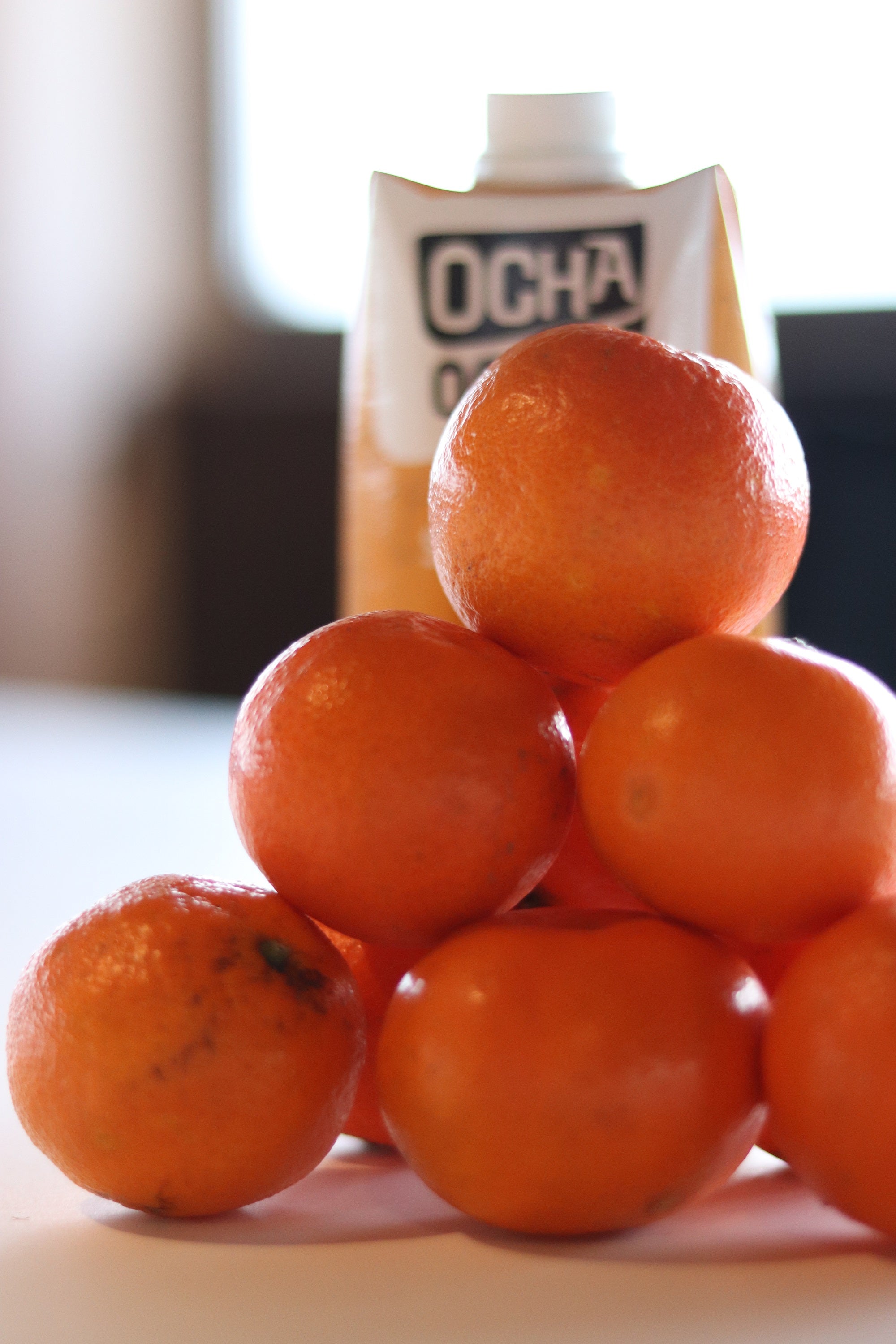 Ein 6er Stapel Mandarinen, dahinter versteckt sich ein Erfrischungsgetränk von Ocha-Ocha